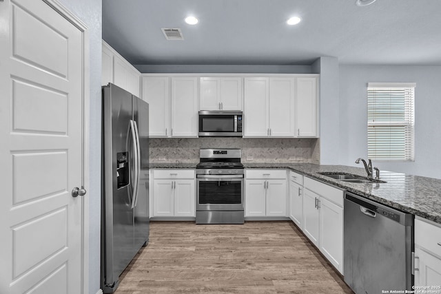 kitchen with stainless steel appliances, visible vents, white cabinetry, a sink, and dark stone counters