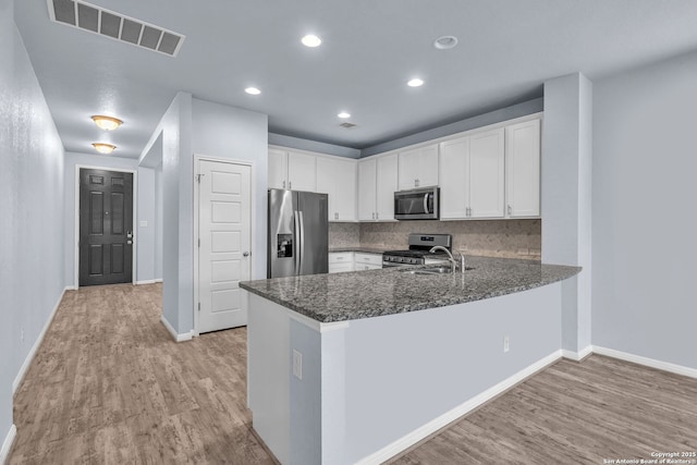 kitchen with a peninsula, appliances with stainless steel finishes, visible vents, and white cabinetry