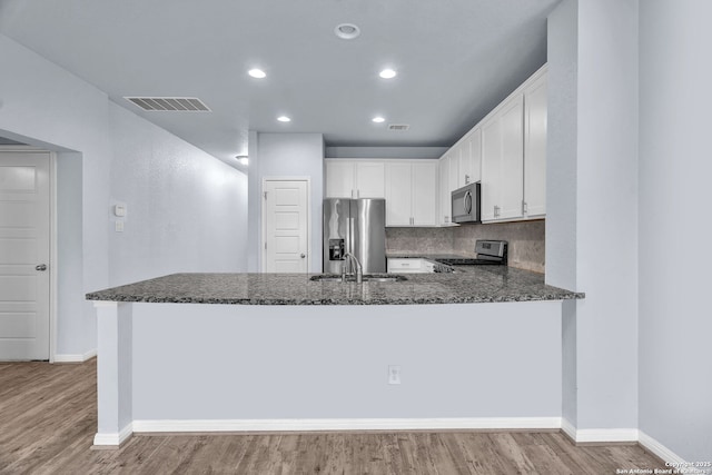 kitchen featuring visible vents, appliances with stainless steel finishes, white cabinets, dark stone countertops, and a peninsula