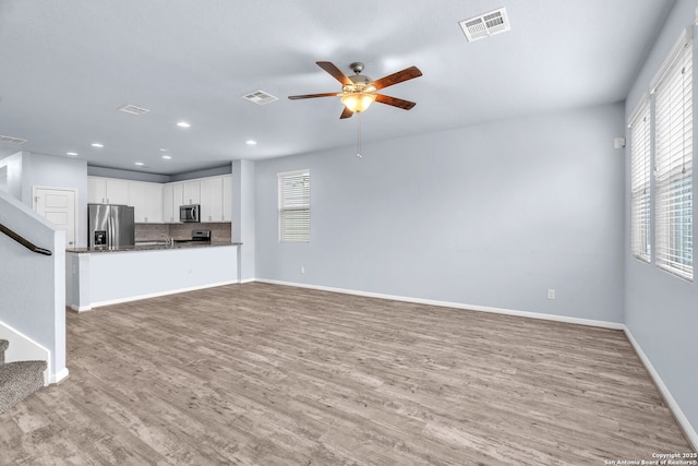 unfurnished living room with a ceiling fan, baseboards, stairs, visible vents, and light wood-style floors