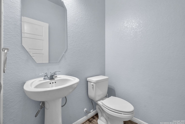 bathroom featuring baseboards, a textured wall, toilet, and wood finished floors