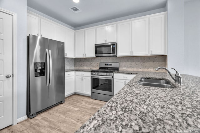 kitchen featuring stainless steel appliances, a sink, visible vents, white cabinets, and light stone countertops