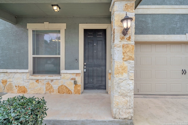 entrance to property with a garage, stone siding, and stucco siding