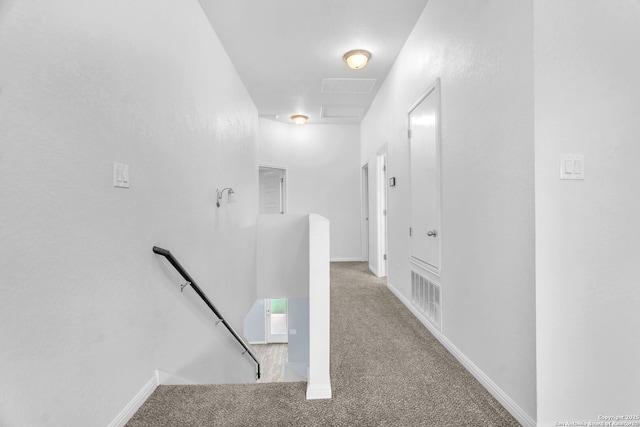 hallway featuring baseboards, carpet flooring, visible vents, and an upstairs landing