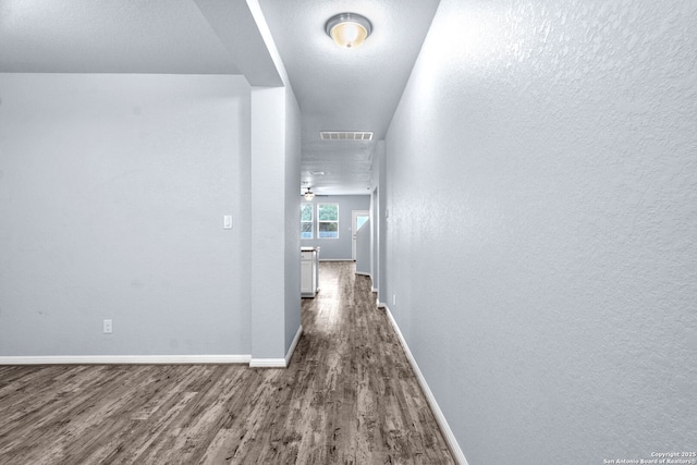 hallway featuring visible vents, baseboards, and dark wood-style flooring