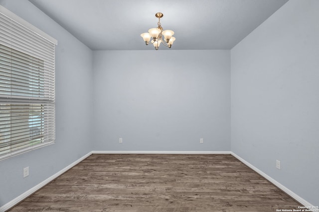 unfurnished room with a chandelier, baseboards, and wood finished floors