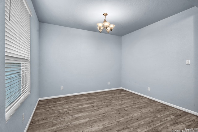 unfurnished room with an inviting chandelier, baseboards, and dark wood finished floors