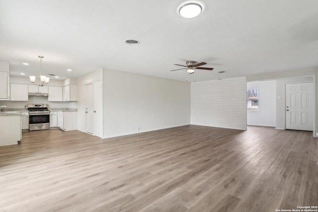 unfurnished living room with ceiling fan with notable chandelier, light wood-style flooring, visible vents, and recessed lighting