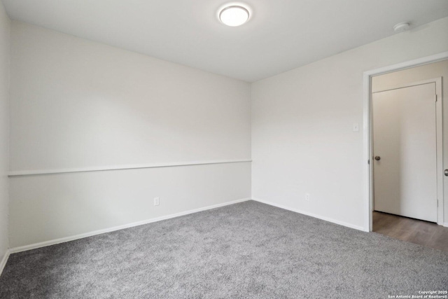 spare room with baseboards and dark carpet