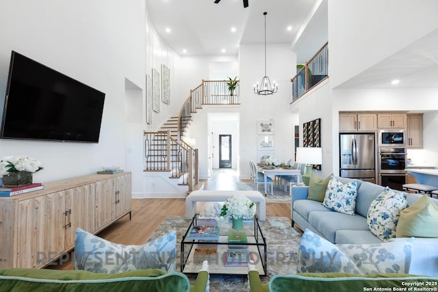 living area featuring light wood-style floors, a high ceiling, stairway, and a chandelier