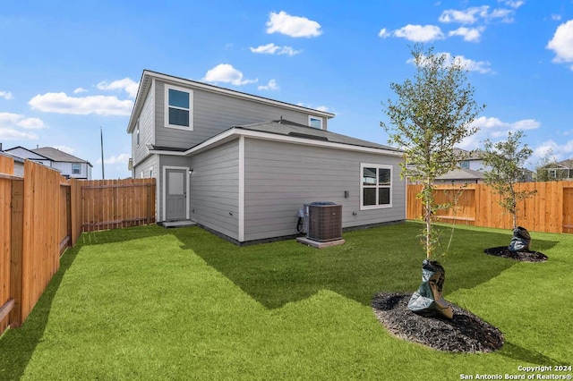 rear view of house with central AC, a lawn, and a fenced backyard