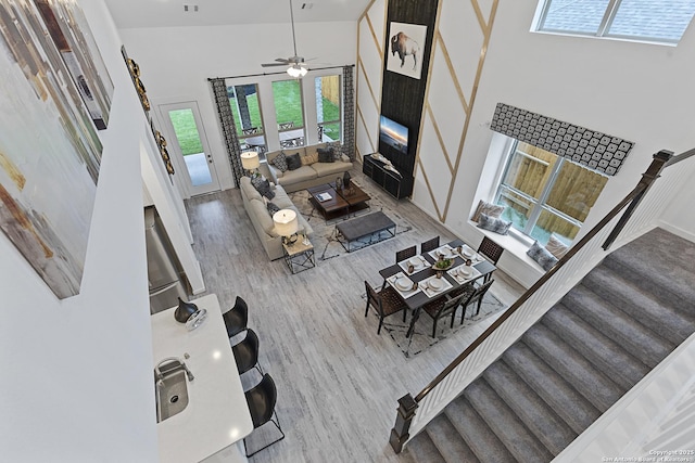 living area featuring stairs, a high ceiling, wood finished floors, and a ceiling fan