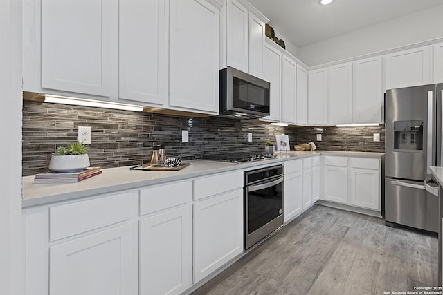 kitchen with appliances with stainless steel finishes, white cabinets, light countertops, and tasteful backsplash