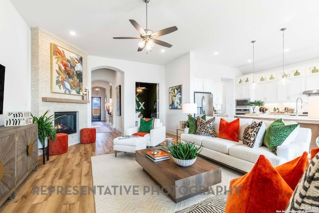 11717 Warlock, San Antonio, TX 78254 - living room featuring a ceiling fan, light wood finished floors, arched walkways, a large fireplace, and recessed lighting