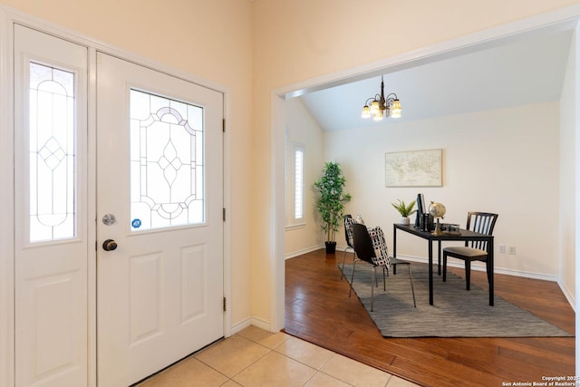 foyer entrance featuring vaulted ceiling, light wood-style floors, baseboards, and an inviting chandelier