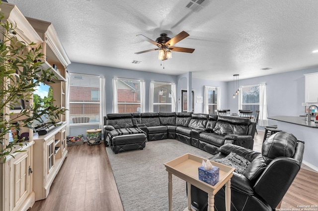 living room featuring ceiling fan, a textured ceiling, wood finished floors, and visible vents