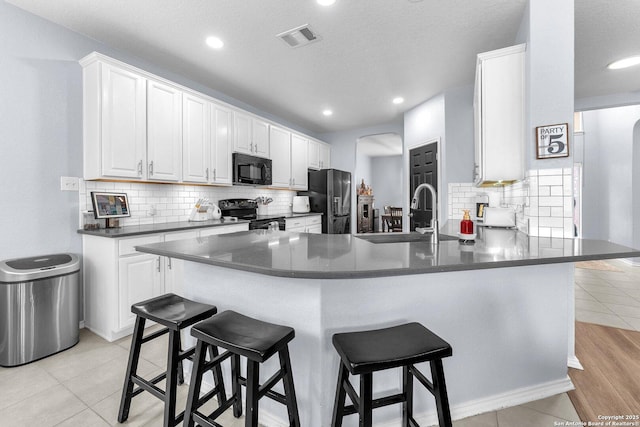 kitchen with a peninsula, a sink, visible vents, black appliances, and dark countertops