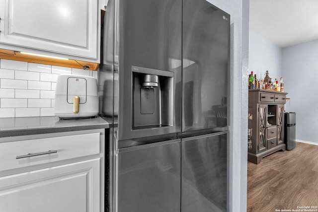 room details featuring dark wood-style flooring, white cabinets, stainless steel refrigerator with ice dispenser, backsplash, and dark countertops