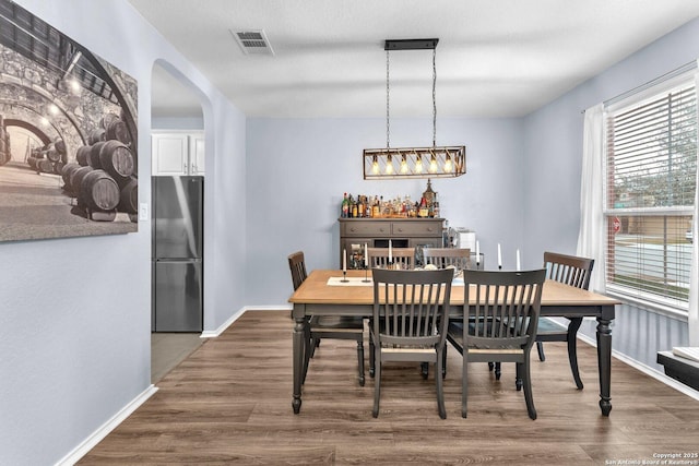 dining area with baseboards, visible vents, arched walkways, and dark wood-style flooring