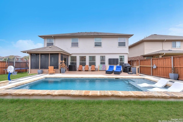 rear view of house with a lawn, a fenced backyard, a sunroom, and a fenced in pool