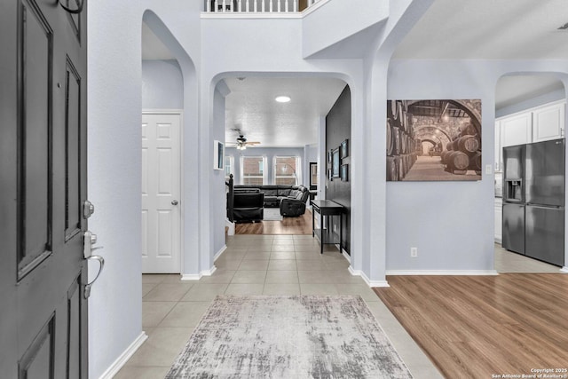 foyer with ceiling fan, light wood-style floors, arched walkways, and baseboards