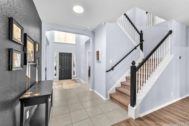 foyer entrance featuring arched walkways, tile patterned flooring, a high ceiling, baseboards, and stairs