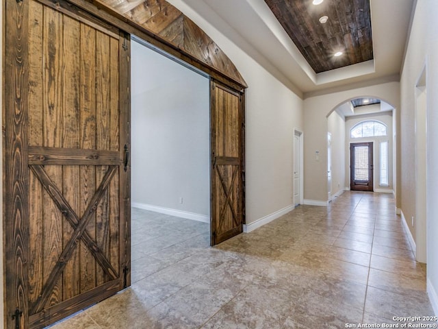 foyer entrance with baseboards, arched walkways, a raised ceiling, and recessed lighting