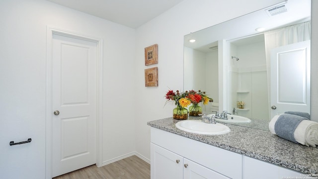 bathroom with visible vents, vanity, wood finished floors, baseboards, and walk in shower