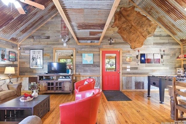 living area with wooden walls, a ceiling fan, wood finished floors, and beamed ceiling