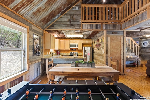 rec room featuring visible vents, a sink, wooden walls, wood finished floors, and high vaulted ceiling