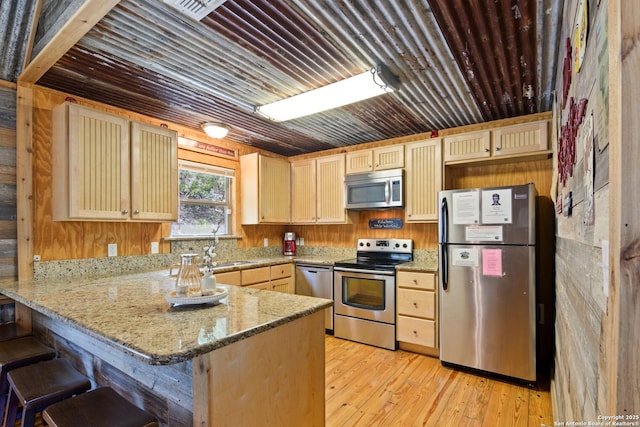 kitchen with light stone counters, appliances with stainless steel finishes, light wood-style floors, light brown cabinets, and a peninsula