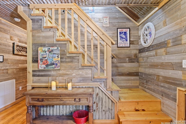 stairs featuring lofted ceiling, visible vents, wooden walls, and wood finished floors