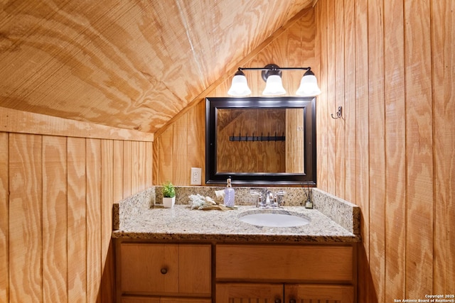 bathroom featuring wooden walls, lofted ceiling, wood ceiling, and vanity