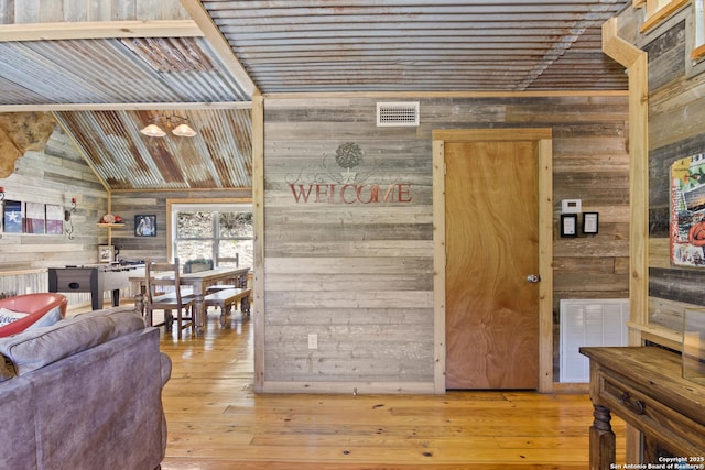 interior space with visible vents, vaulted ceiling, wooden walls, and wood finished floors