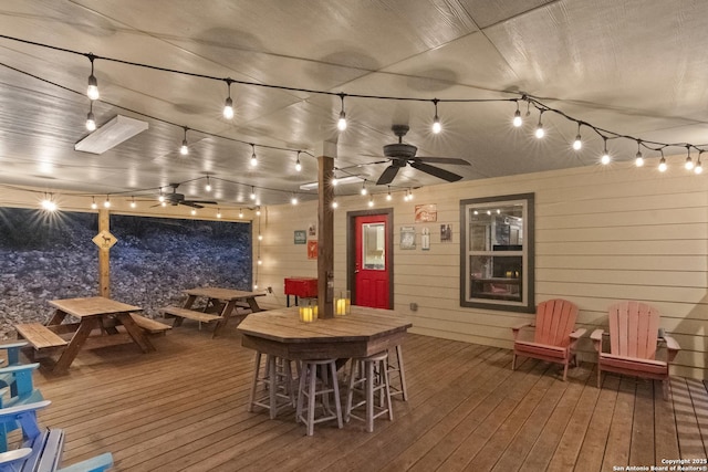 wooden deck with exterior bar, ceiling fan, and outdoor dining space