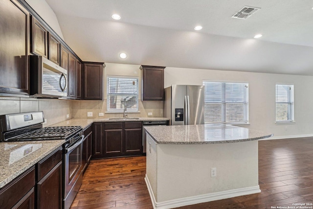 kitchen featuring light stone counters, stainless steel appliances, lofted ceiling, visible vents, and a sink