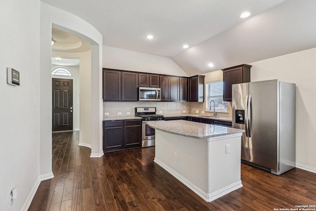 kitchen with dark brown cabinetry, dark wood-style floors, appliances with stainless steel finishes, a center island, and a sink