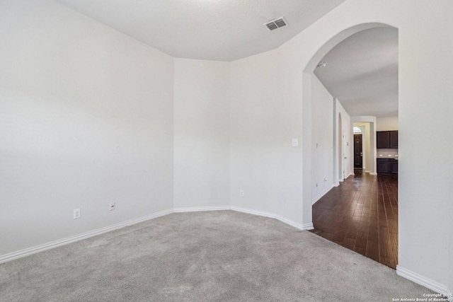 carpeted empty room with visible vents, arched walkways, and baseboards