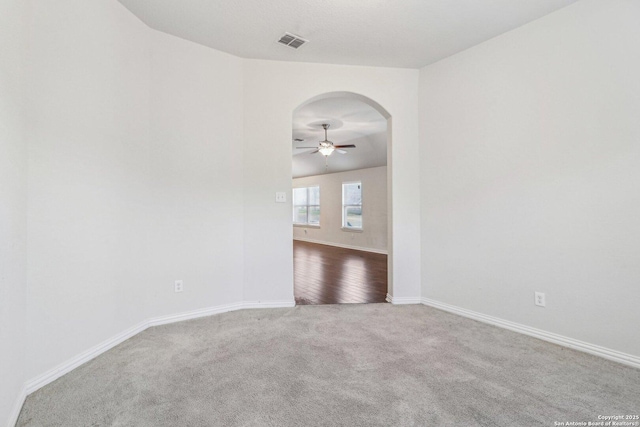 carpeted empty room with arched walkways, visible vents, ceiling fan, and baseboards