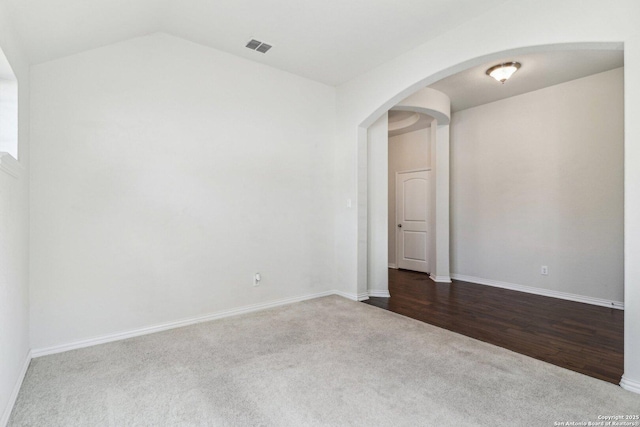 empty room featuring visible vents, arched walkways, baseboards, lofted ceiling, and dark colored carpet