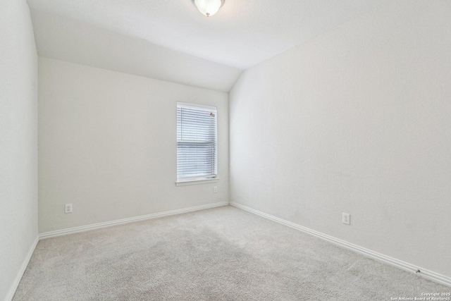 unfurnished room with light carpet, vaulted ceiling, and baseboards