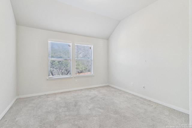 spare room featuring light colored carpet, vaulted ceiling, and baseboards