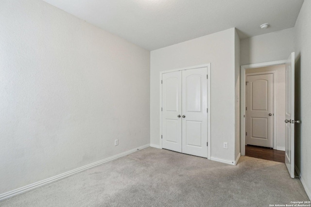 unfurnished bedroom with a closet, light colored carpet, and baseboards