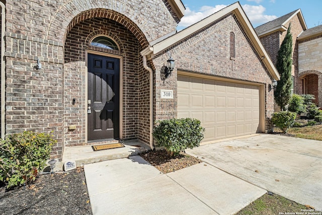 doorway to property featuring a garage, concrete driveway, and brick siding