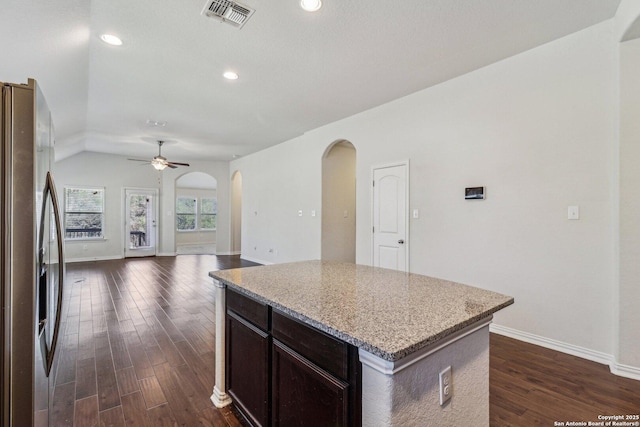 kitchen featuring arched walkways, stainless steel refrigerator with ice dispenser, visible vents, open floor plan, and a kitchen island