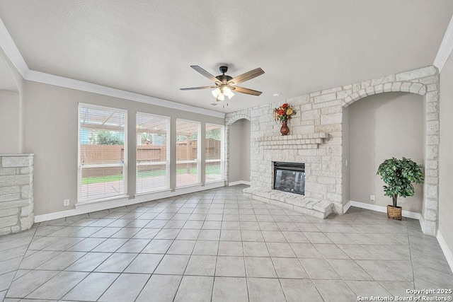 unfurnished living room featuring light tile patterned floors, baseboards, a ceiling fan, ornamental molding, and a stone fireplace