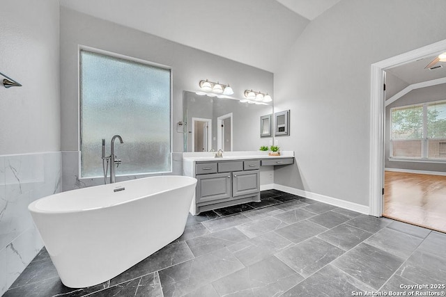 bathroom featuring lofted ceiling, a soaking tub, vanity, and tile walls