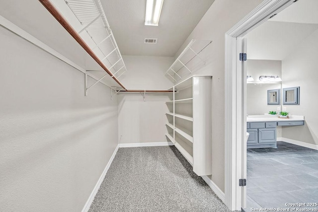 walk in closet with carpet floors, visible vents, and built in desk