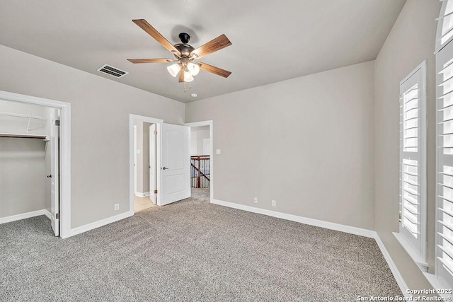unfurnished bedroom featuring a walk in closet, visible vents, a ceiling fan, carpet flooring, and baseboards