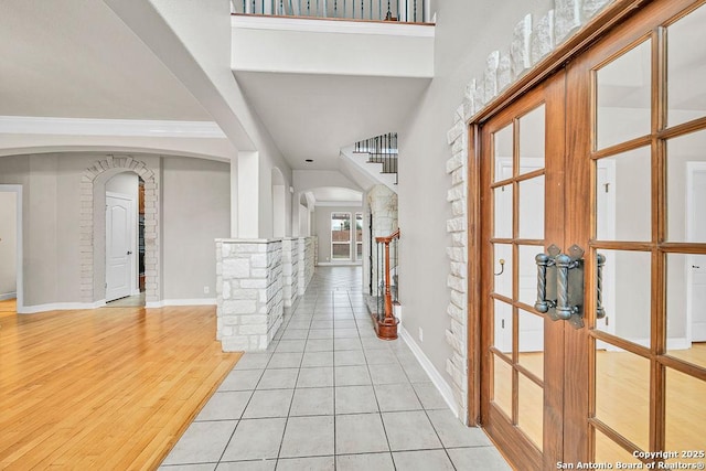 entrance foyer featuring arched walkways, baseboards, stairs, and light wood-style floors